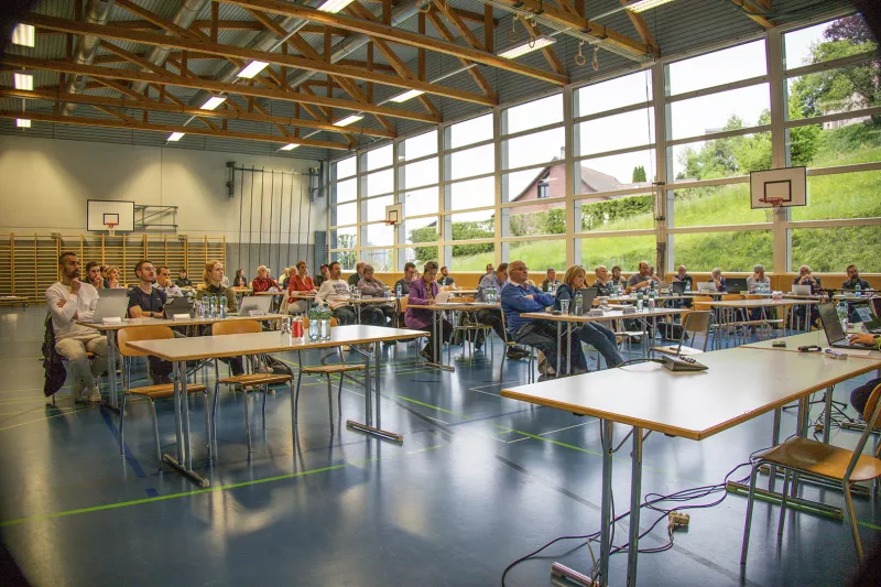 Séance du Conseil général dans une salle de sport, les conseillers assis à des tables